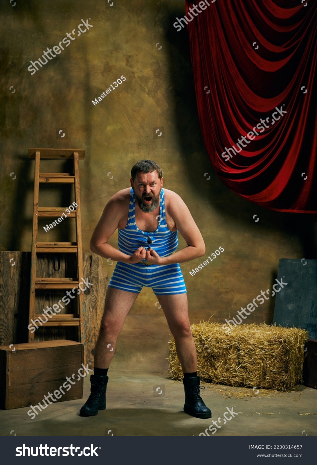 Winner emotions. Mature man, retro circus strongman wearing striped sports swimsuit shouting isolated over dark vintage circus backstage background. Art, 30s, 40s fashion style and inspiration #2230314657