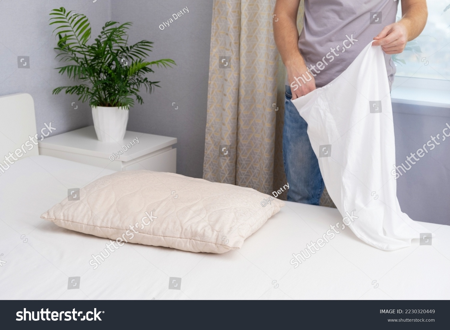 A man tucks a pillow with a fresh bright white pillowcase. Making the bed with fresh bed linen by a white man. The day of the change of bed linen. The day of washing bed linen in the laundry room. #2230320449