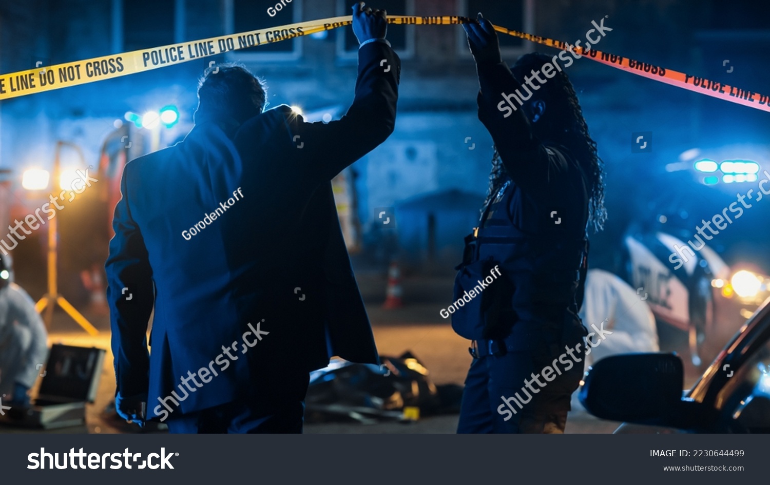 Team of Two Multiethnic Police Officers Working on Profiling a Killer on the Loose. Detectives on Duty at Night Solving Crime to Bring a Violent Murderer to Justice. Police Car and Paramedics on Site #2230644499