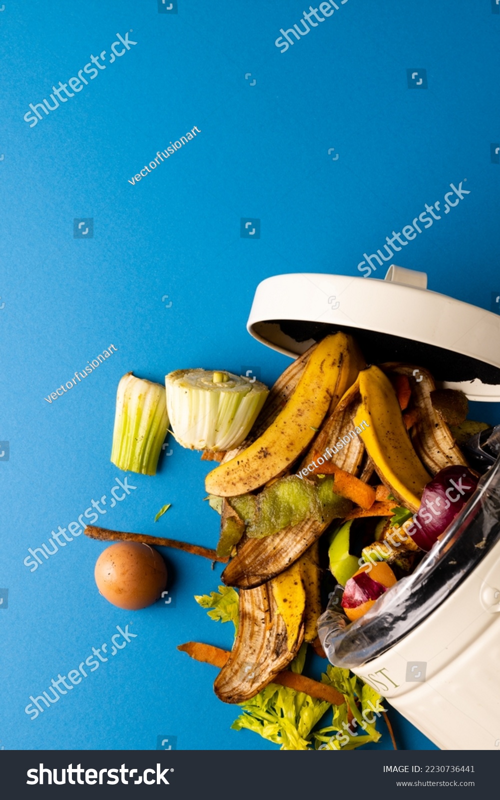 Vertical image of organic fruit and vegetable food waste spilling from open kitchen composting bin. On blue background with copy space. Ecology, recycling, care and nature concept. #2230736441