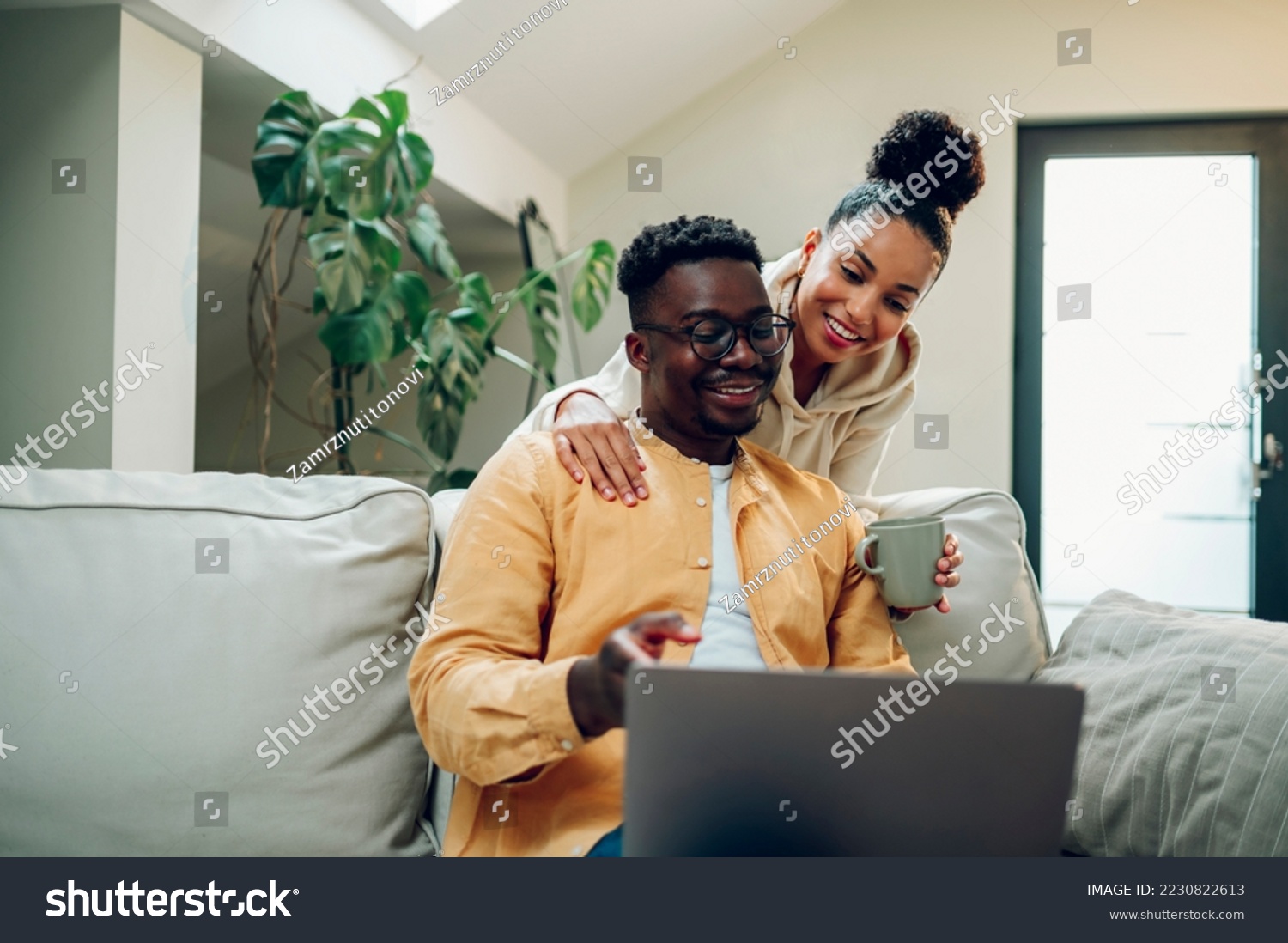 Portrait of a diverse couple enjoying time at home and using laptop. African american man and hispanic woman hugging and looking into the screen. Modern interior. Copy space. #2230822613