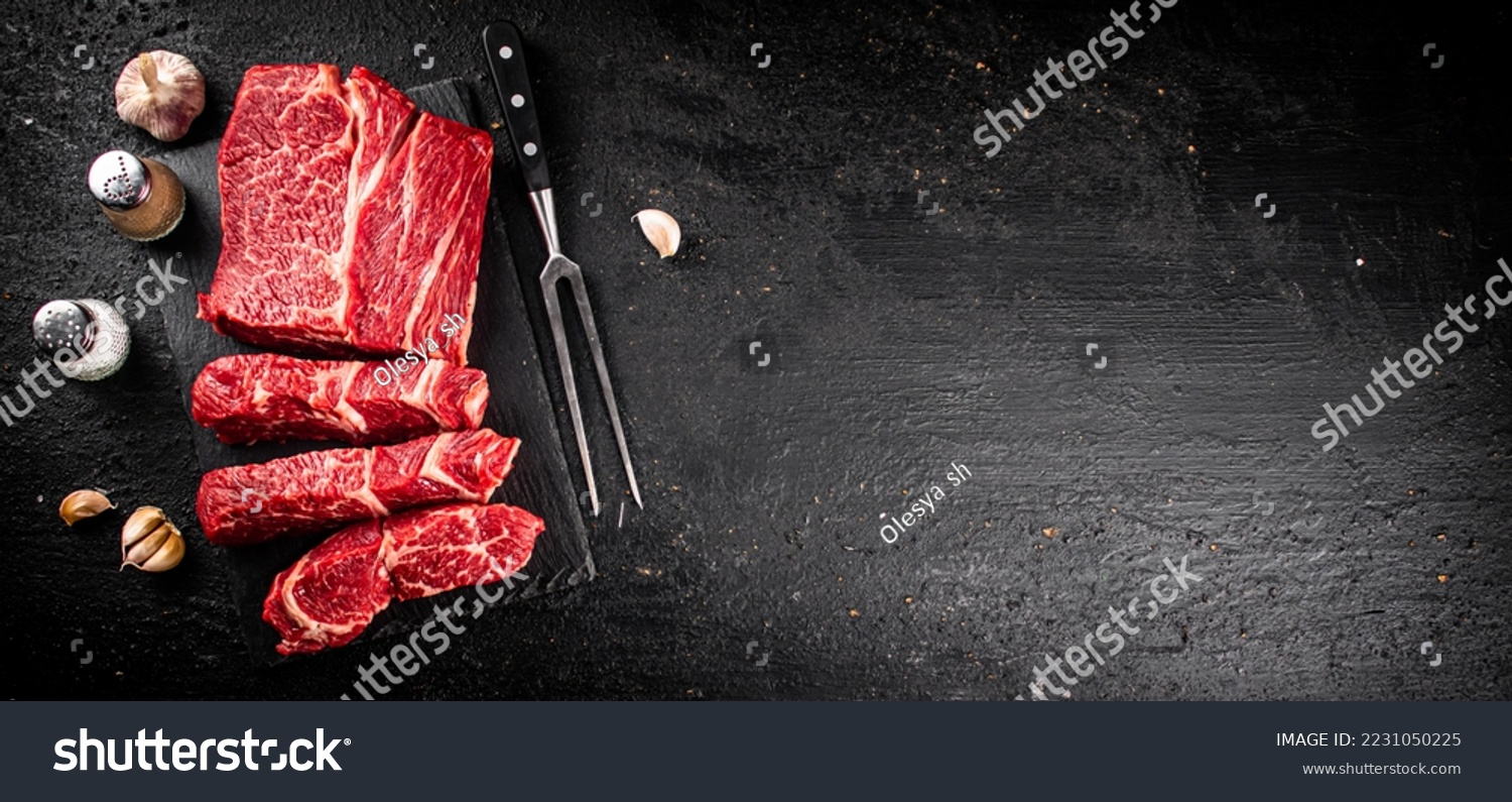 Pieces of raw beef on a stone board. On a black background. High quality photo #2231050225