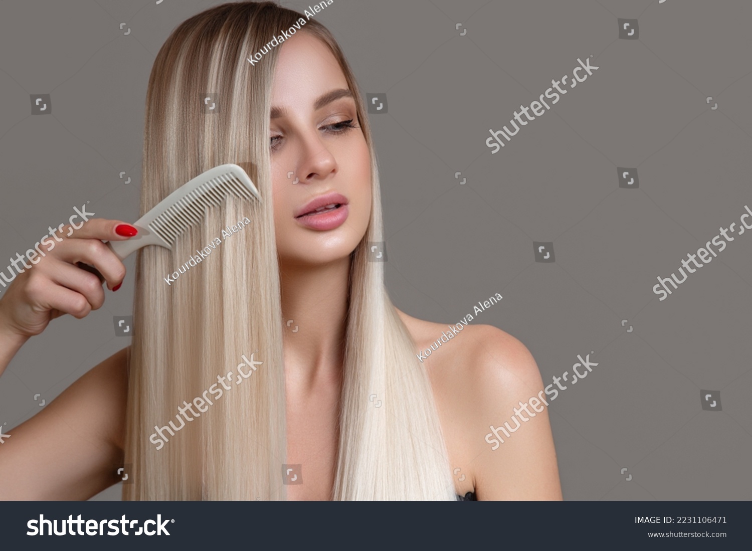 beautiful young woman holds a comb in her hands. Blonde woman with long straight hair on a gray background #2231106471