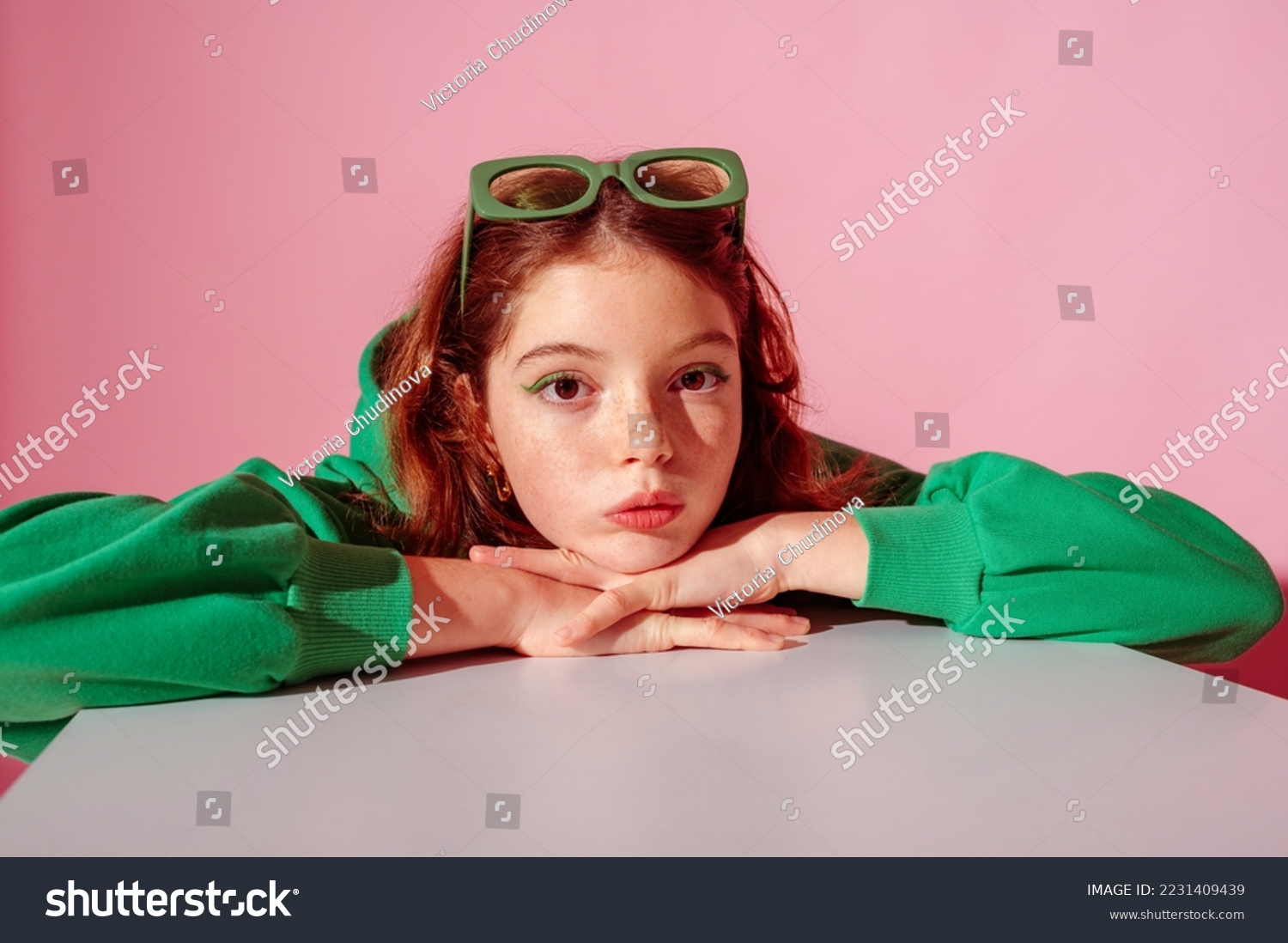 Beautiful freckled redhead girl wearing trendy green hoodie, posing against pink background. Close up studio portrait. Copy, empty space for text
 #2231409439