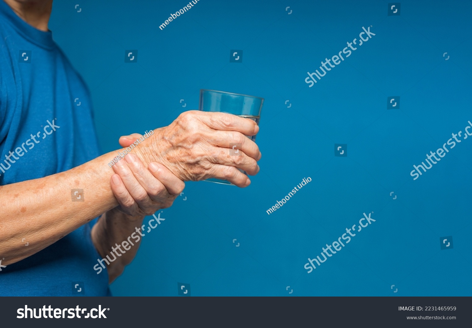Close-up of hands senior woman trying to hold a glass of water. Causes of hand shaking include Parkinson's disease, stroke, or brain injury. Mental health neurological disorder #2231465959