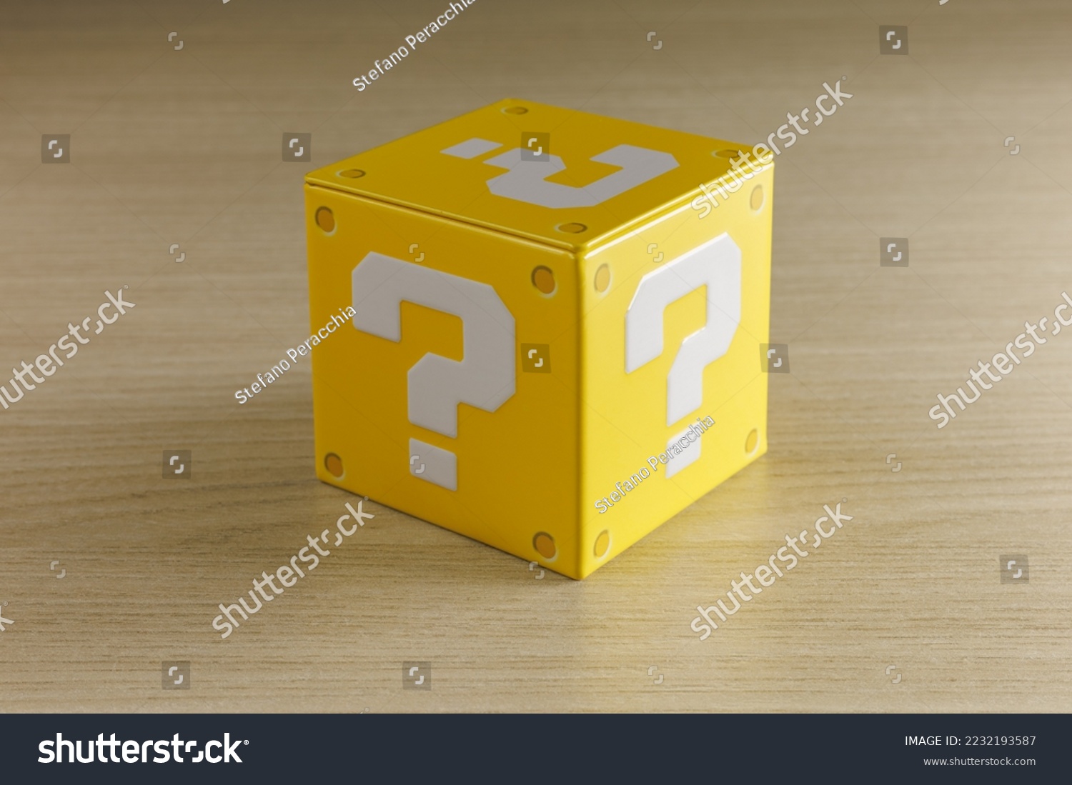 Indoor still-life photo of a little yellow box with a big white question mark printed on each face. It recalls a graphic element of a famous platform video game. #2232193587