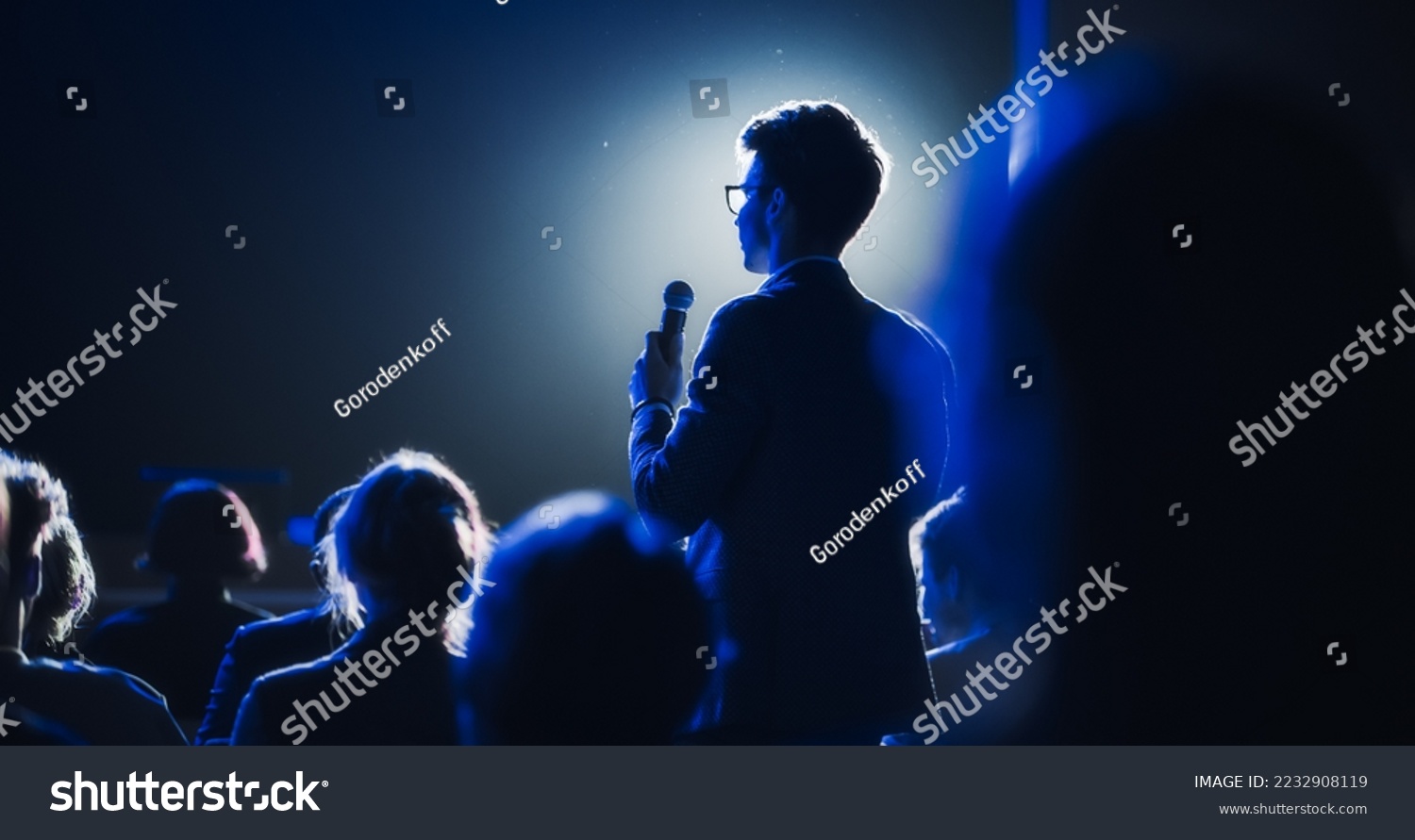 Male Asking a Question to a Speaker During a Q and A Session at an International Tech Conference in a Dark Crowded Auditorium. Young Specialist Expressing an Opinion During a Global Business Summit. #2232908119