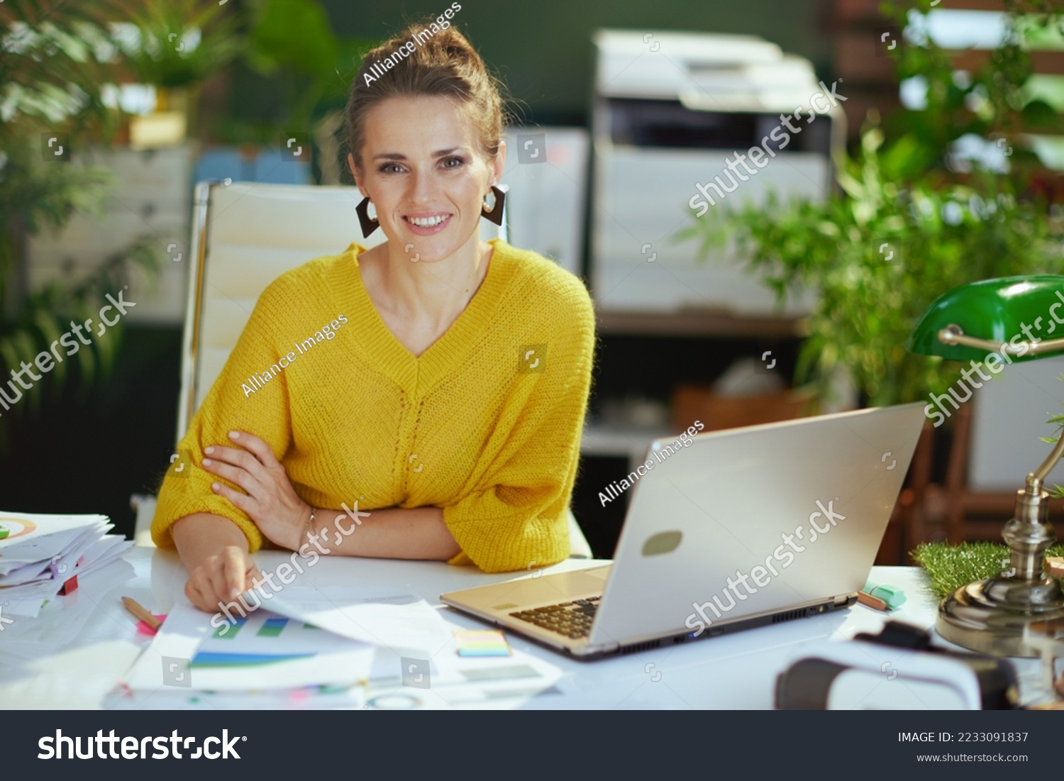 happy elegant 40 years old small business owner woman in yellow sweater with laptop working with documents in the modern green office. #2233091837