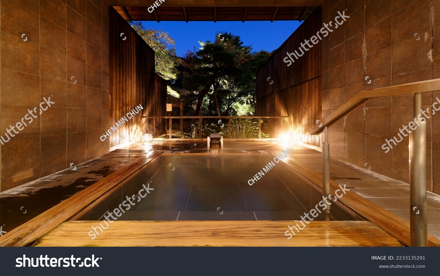 A Japanese-style open-air Kashikiri Buro (a charter hot-spring bath) in a Ryokan, with a wooden bathtub illuminated at blue dusk and a relaxing vibe in the natural setting of a green forest #2233135291