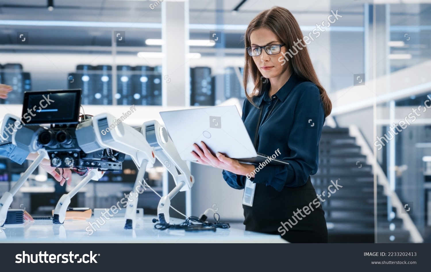 Portrait of a Young Robotics Engineer Using Laptop Computer, Analyzing Robotic Machine Concept in a High Tech Factory. Female Scientist Manipulate and Program the Robot for Work. #2233202413