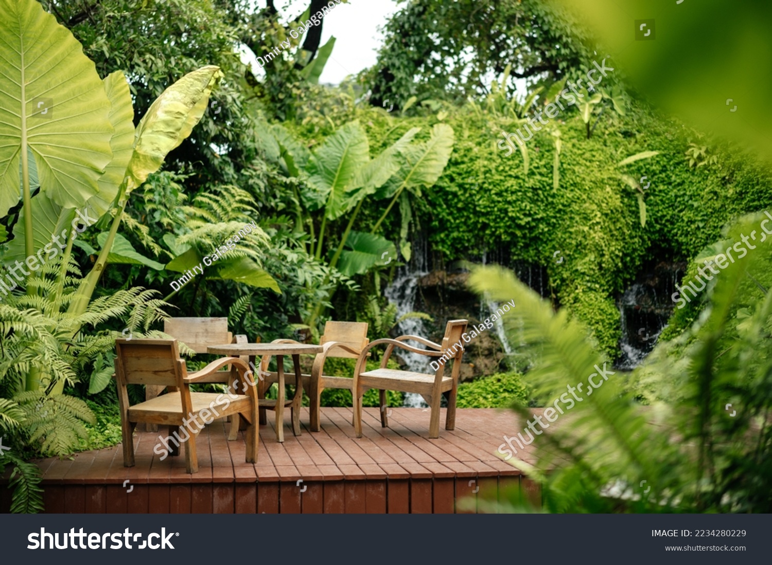 Wooden chairs and tables on the street in the tropics among the foliage. Exterior of cafe or lounge zone. #2234280229