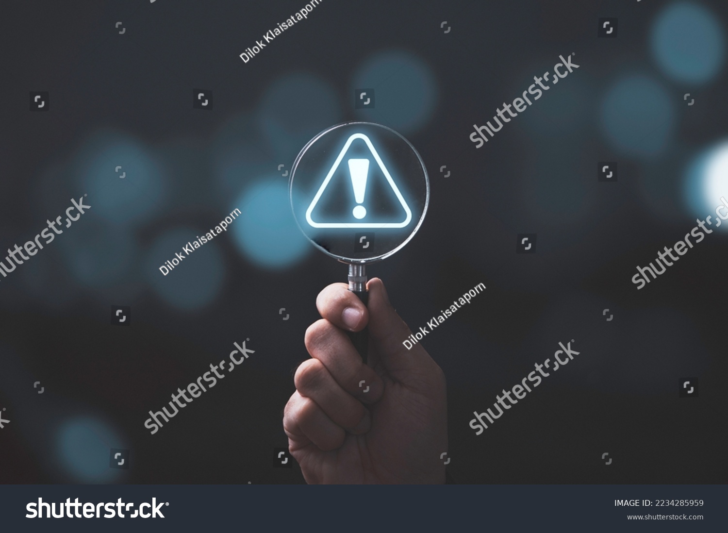 Hand holding magnifier glass with red triangle caution warning sign for notification error and maintenance concept. #2234285959