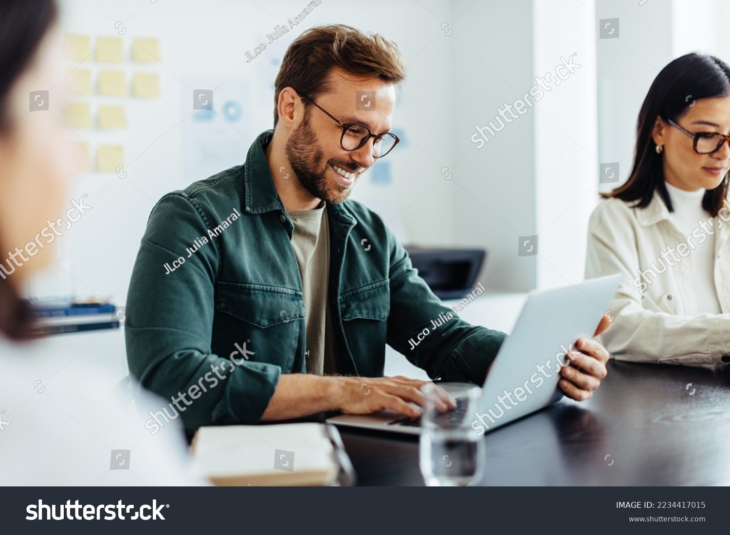 Designer using a laptop during a meeting in an office. Happy business man reading an email while sitting in a boardroom with his colleagues. #2234417015