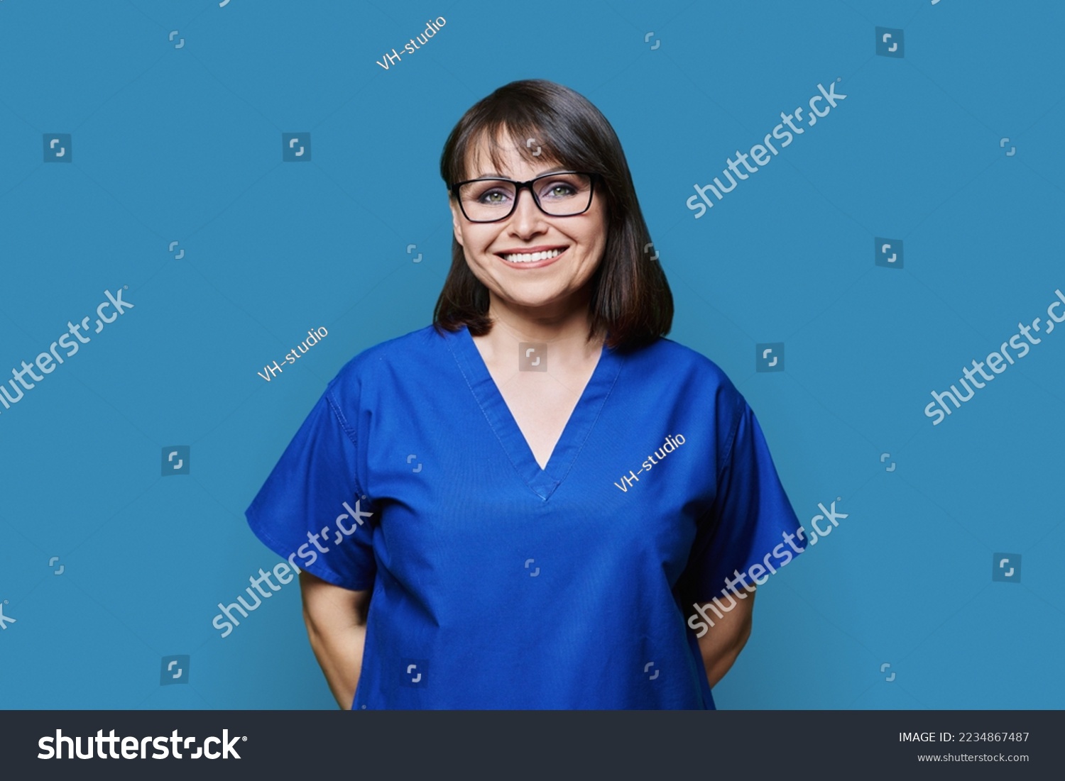 Smiling woman in blue scrubs uniform looking at camera on blue background #2234867487