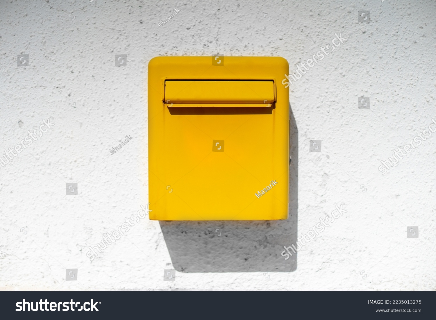 Yellow bright metal mailbox hangs on white rough wall casting shadow from sun. Stylish detail in interior of house authentic street box for letters postcards. Background good news holiday messages #2235013275