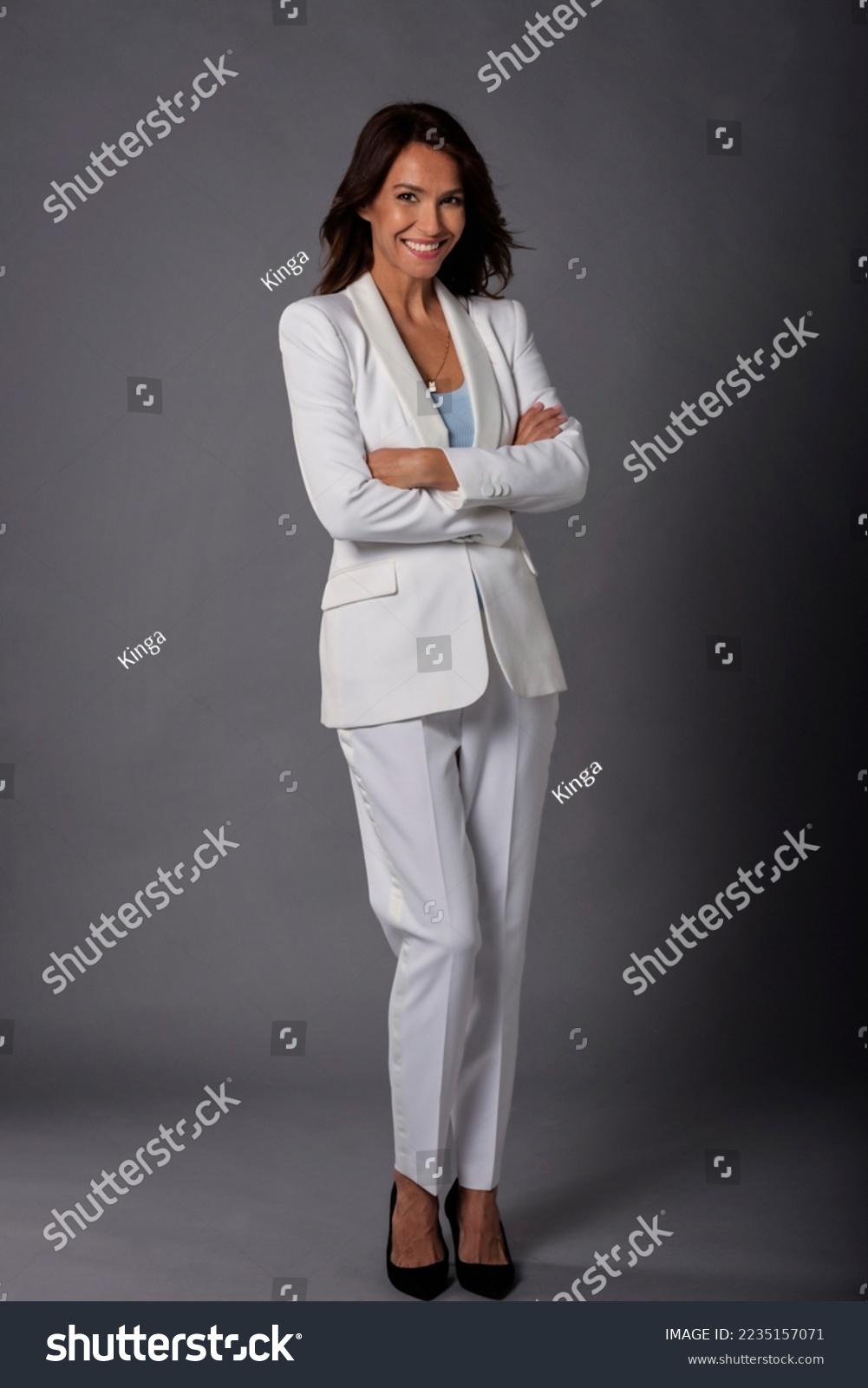 Close-up of an attractive middle aged woman with toothy smile wearing blazer while sitting at isolated dark background. Copy space. Studio shot. #2235157071