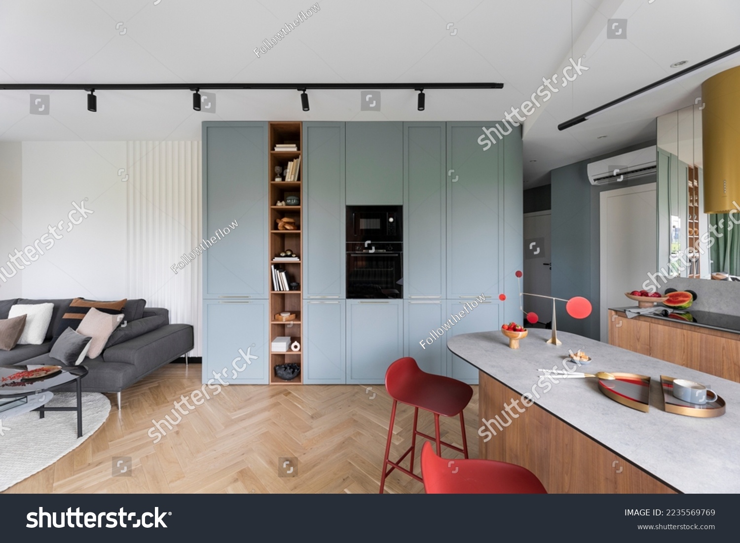 Interior design of colorful open space with built-in oven, bookcase, modern red hockers, wooden kitchen island, gray sofa, pillows, panels floor and personal accessories. Home decor. Template. #2235569769