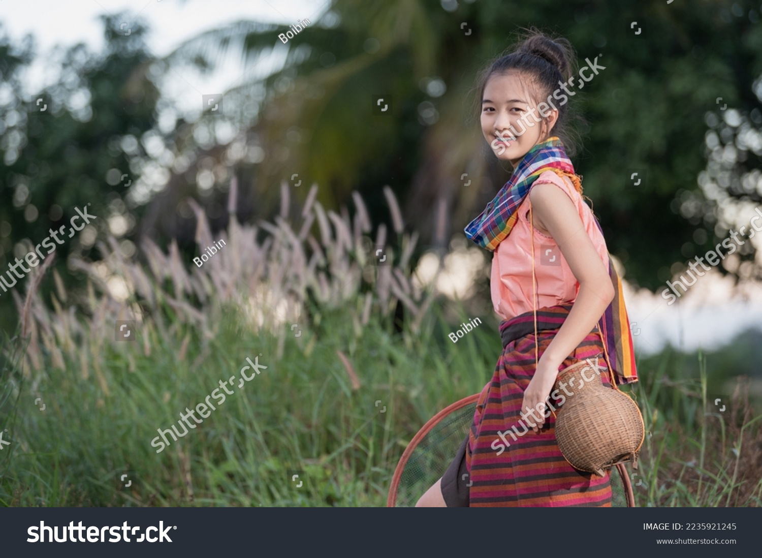 A young Asian farmer girl (with braces) smiling cheerfully as she prepares to fish in a pond beside the rice field. #2235921245