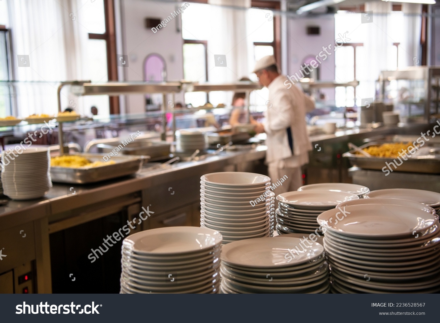 A pile of plates infront of Staff worker preparing food for students in school canteen. Lunch break. Education people and students school cafeteria. Belgrade, Serbia 17.05.2022
 #2236528567