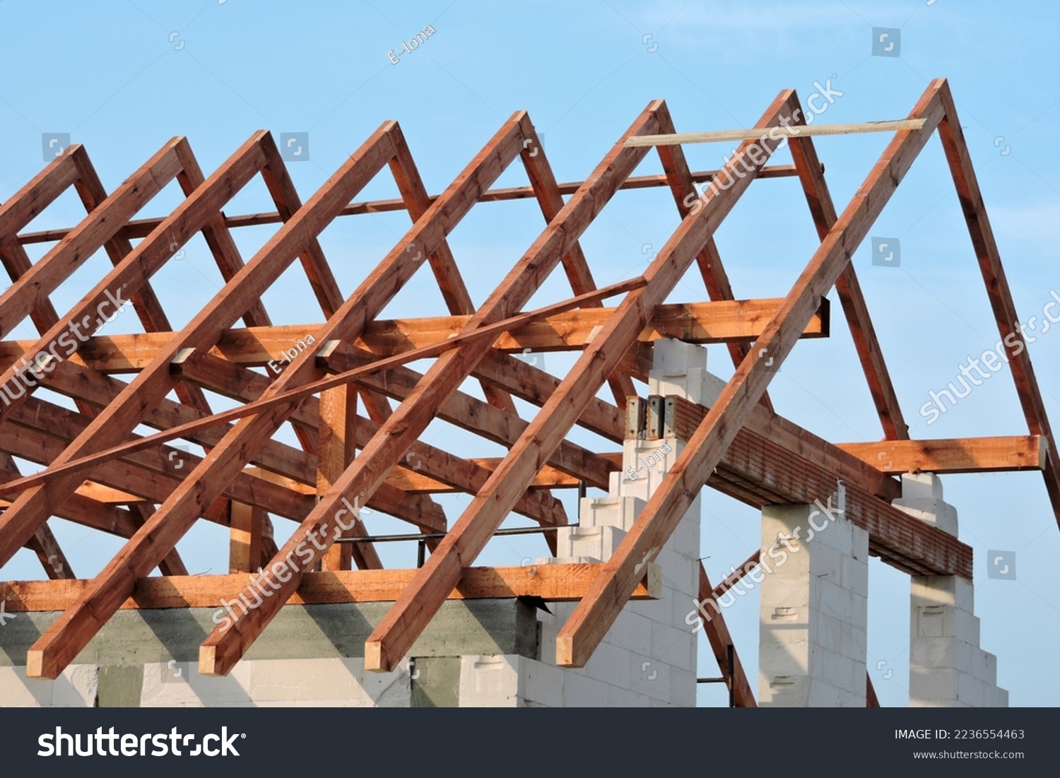 A timber roof truss, walls made of autoclaved aerated concrete blocks, a reinforced concrete beam and columns, a rough window opening, reinforced brick lintels, blue sky in the background #2236554463