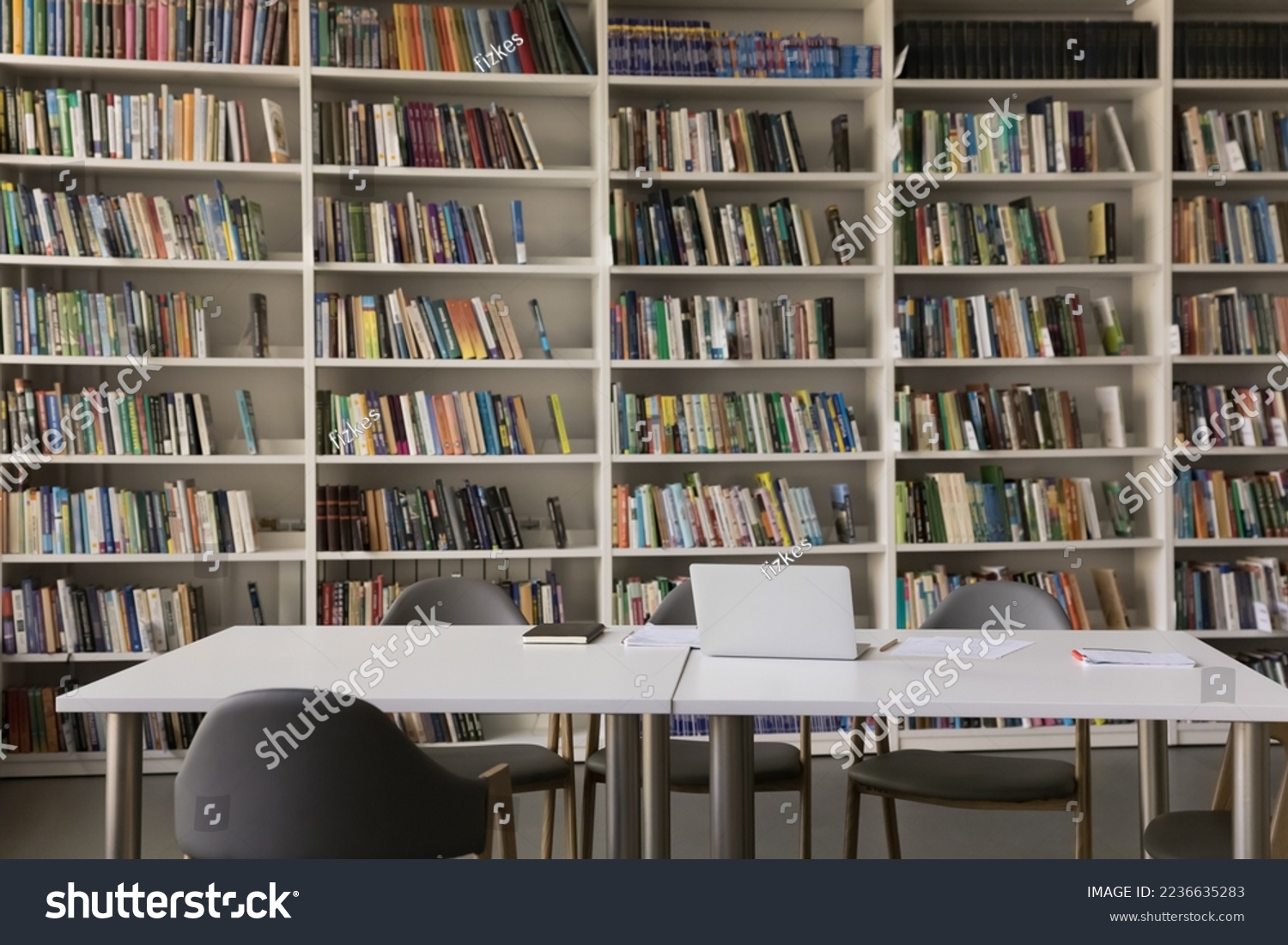 Public library interior with no people and bookshelves. Workplace table, desk with laptop and chairs for studying, college, university, high school students self preparation #2236635283