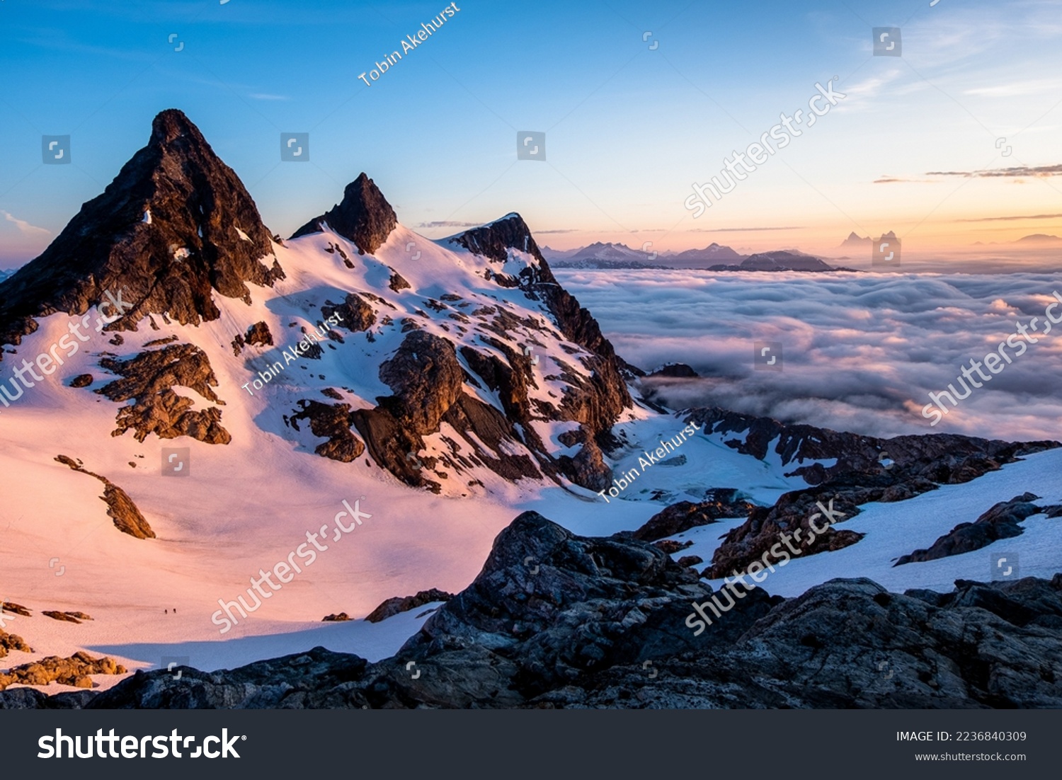 Sunrise Illuminates an Ocean of Clouds and Snowfield Peak as Two Small Climbers Ascend the Glacier Below. 
North Cascades National Park, Washington #2236840309