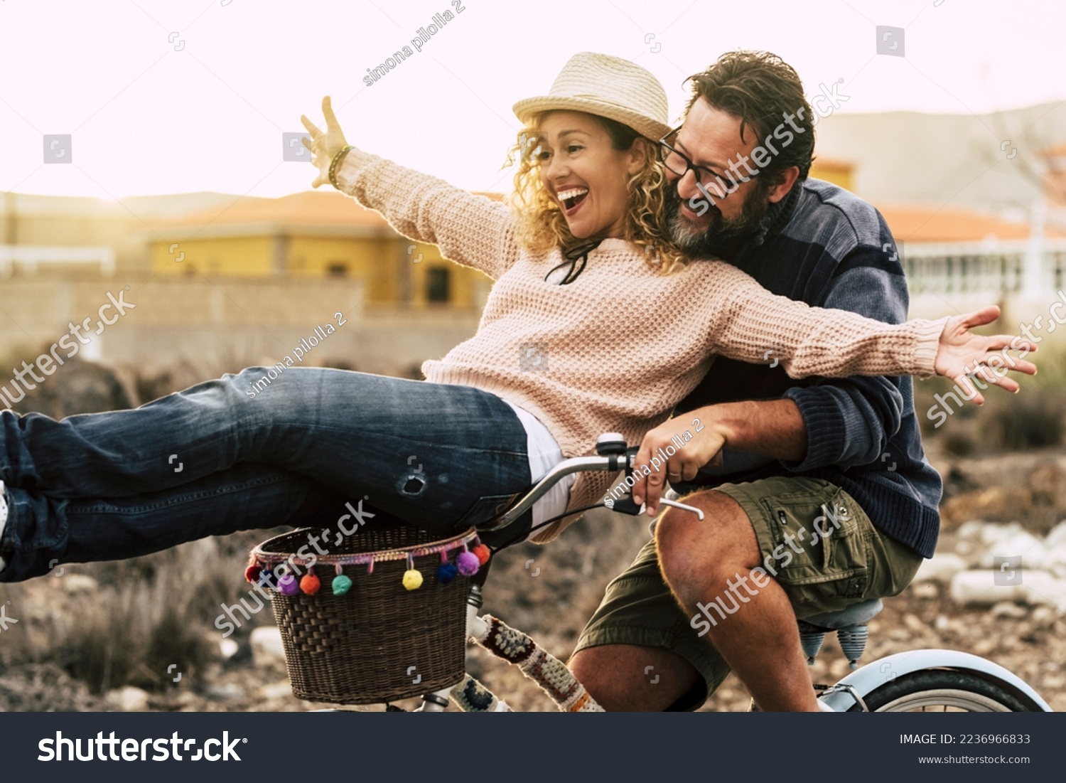 Happy couple enjoy outdoor leisure activity together carrying and using a bike and laughing a lot. Love and friendship with mature man and woman in youthful lifestyle. Concept of joyful and excitement #2236966833