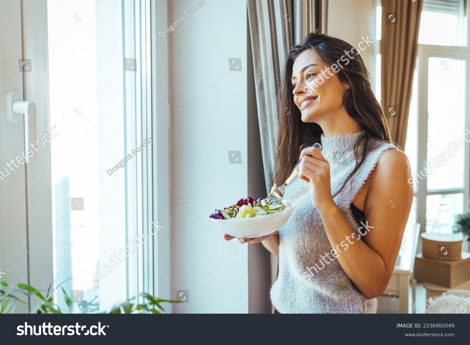 Photo of young woman enjoying a delicious salad at home during the day. Portrait of a young and cheerful woman eating healthy salad. Healthy eating, wellbeing and lifestyle concept #2236982049
