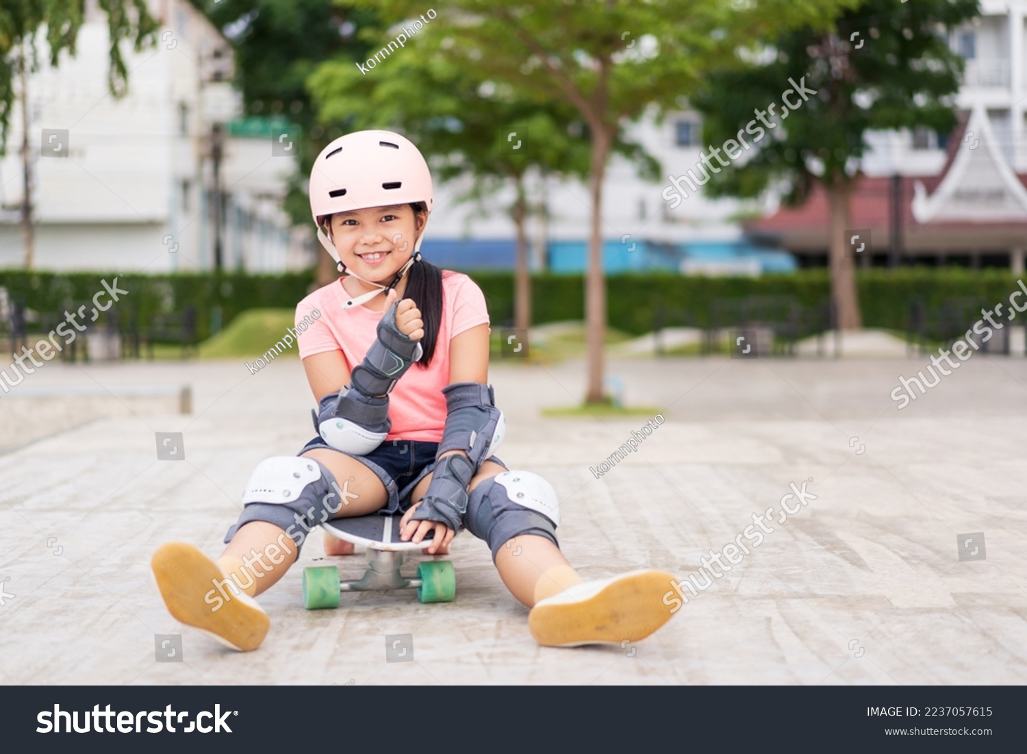 asian child skater or kid girl smile playing skateboard or sitting thumbs up to like on surf skate and fun in skate park for extreme sports to wear helmet elbow wrist knee support for body safety #2237057615
