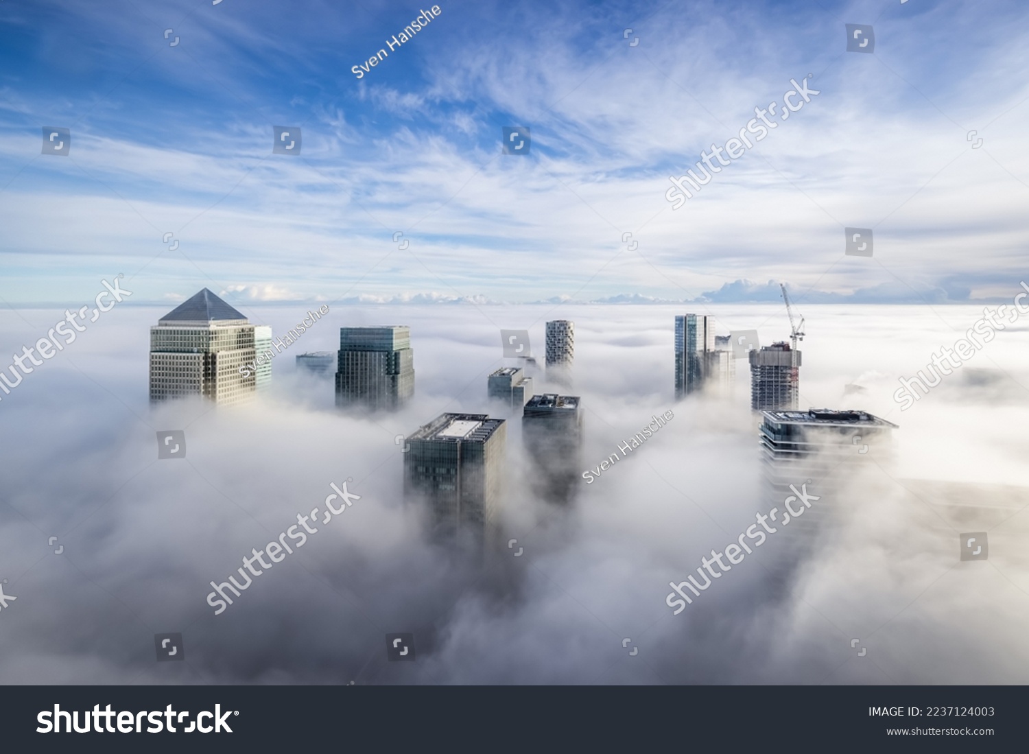 The modern skyline of Canary Wharf, London, during a foggy day with the tops of the skyscrapers looking out of the clouds #2237124003