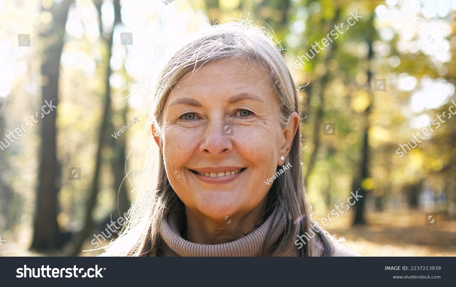 Close-up portrait of naturally beautiful senior cute gray-haired woman standing in park in autumn wearing coat looking at camera smiling. Pretty mature kind good-looking female on fresh air. #2237213939