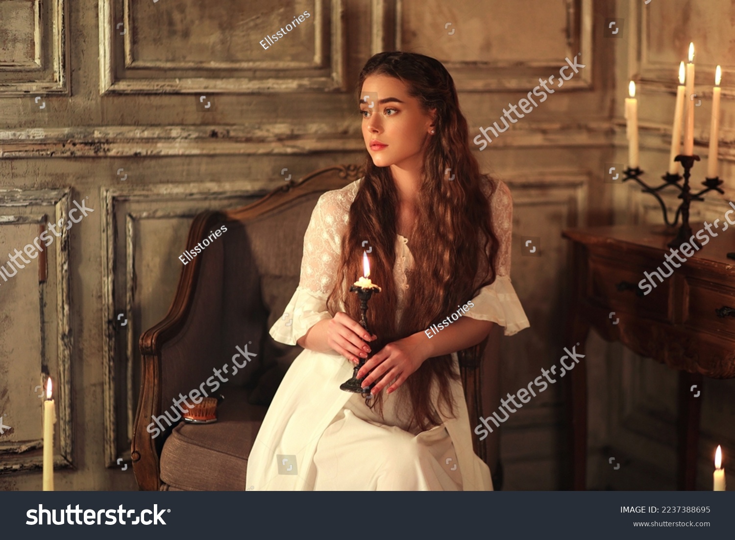 Young long haired woman in vintage night gown sitting on chair with candle in hands. Historic portrait of noble woman #2237388695