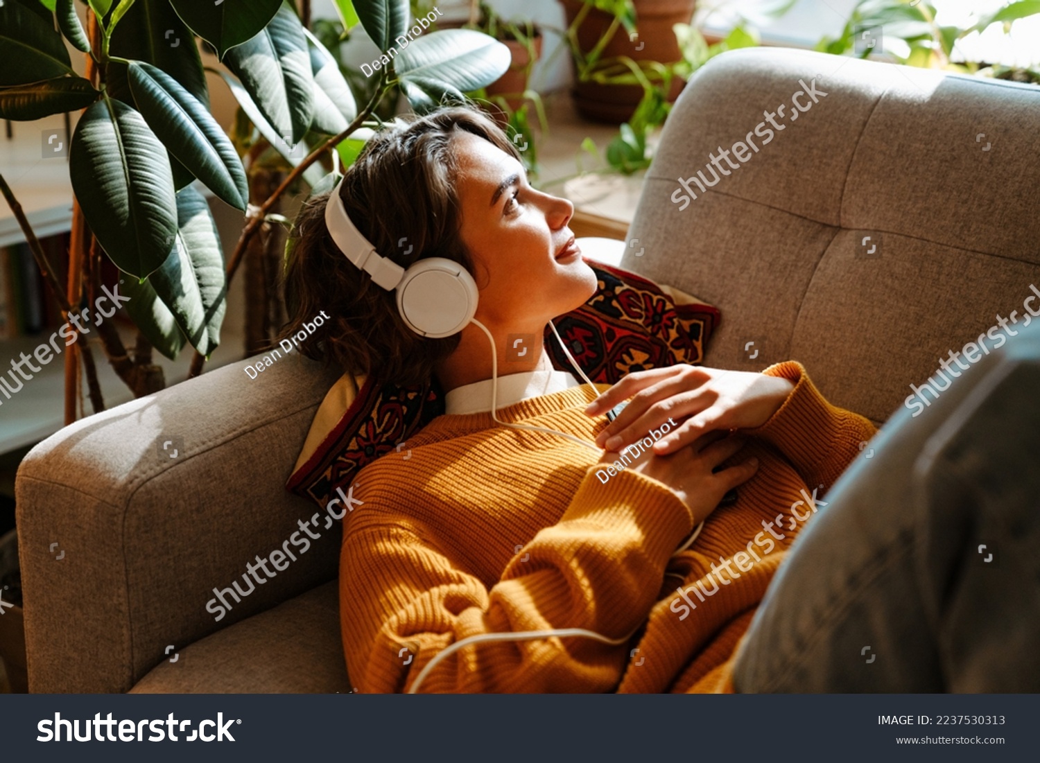 Brunette young woman listening music while resting on couch at home #2237530313