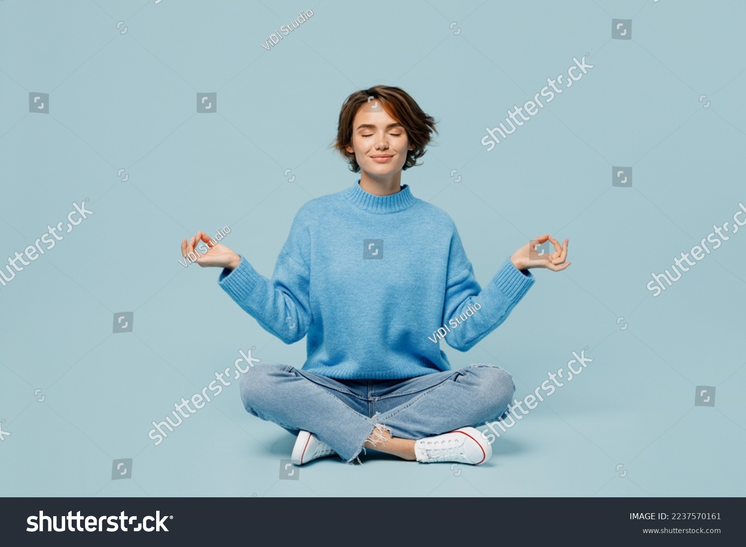 Full body young woman wear knitted sweater holding spreading hands in yoga om aum gesture relax meditate try to calm downisolated on plain pastel light blue cyan background. People lifestyle concept #2237570161