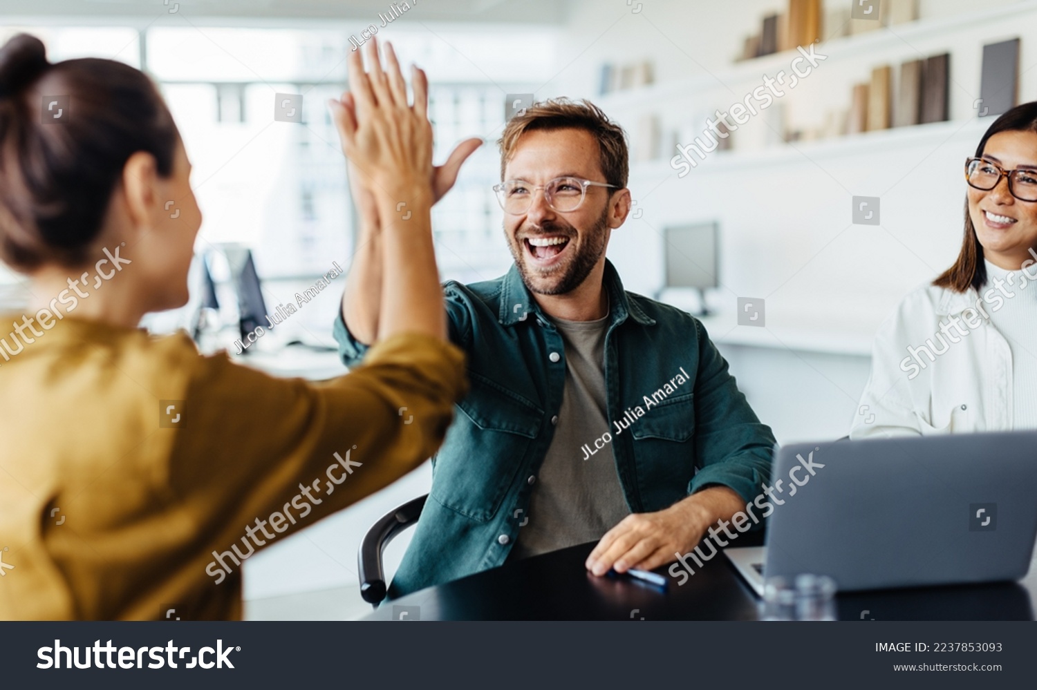 Successful business people giving each other a high five in a meeting. Two young business professionals celebrating teamwork in an office. #2237853093
