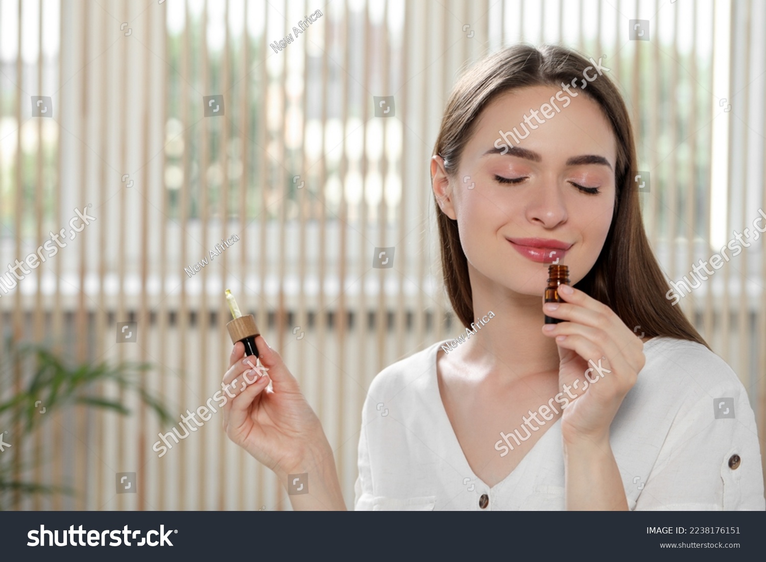 Young woman smelling essential oil indoors, space for text #2238176151