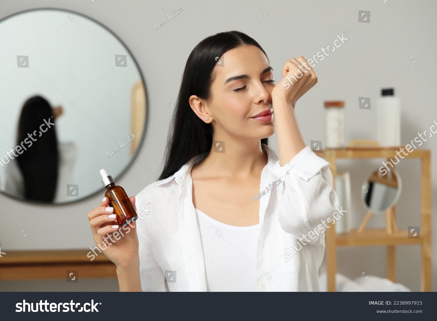 Young woman smelling essential oil on wrist indoors #2238997915