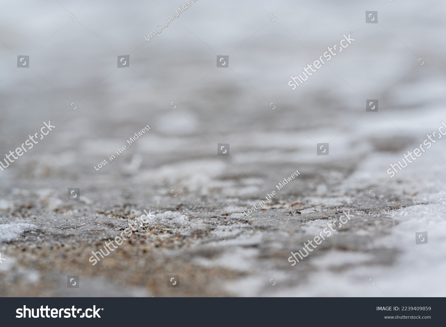 macro ground level closeup view of rock salt ice-melt on concrete with a frozen layer.  #2239409859