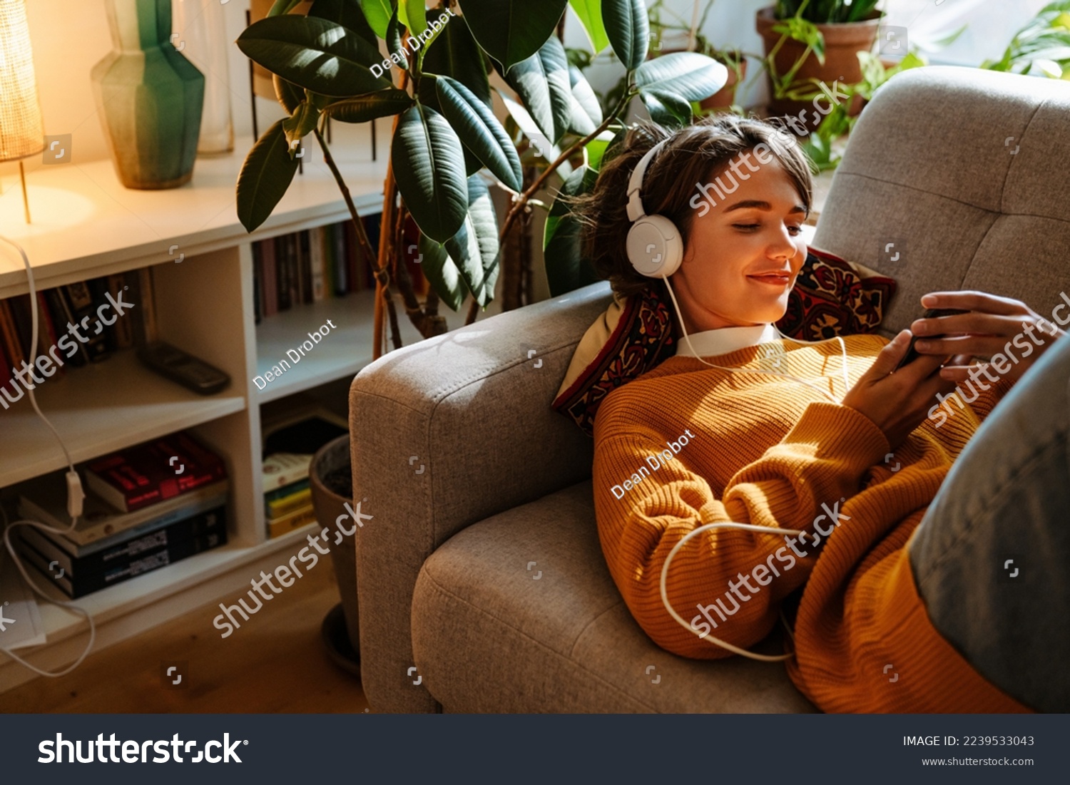 Brunette young woman listening music and using cellphone while resting on couch at home #2239533043