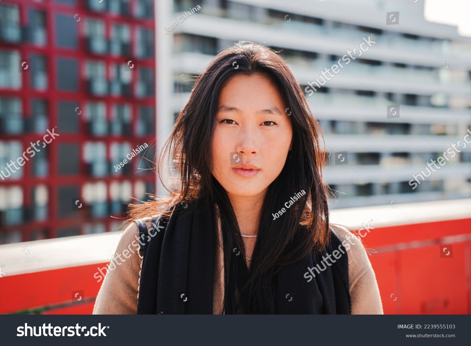 Front view of young stylish chinese woman looking serious at camera. Close up portrait of a relaxed asian lady standing outdoors at city street. High quality photo #2239555103