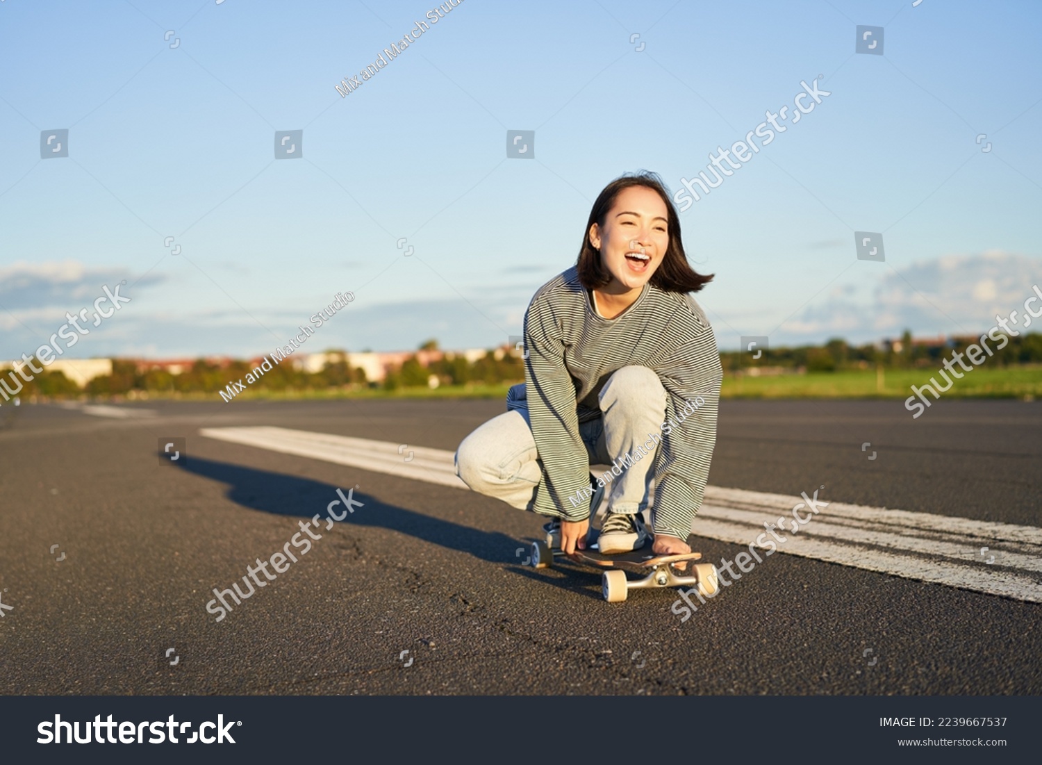 Freedom and happiness. Happy asian girl riding her longboard on an empty sunny road, laughing and smiling, skateboarding. #2239667537