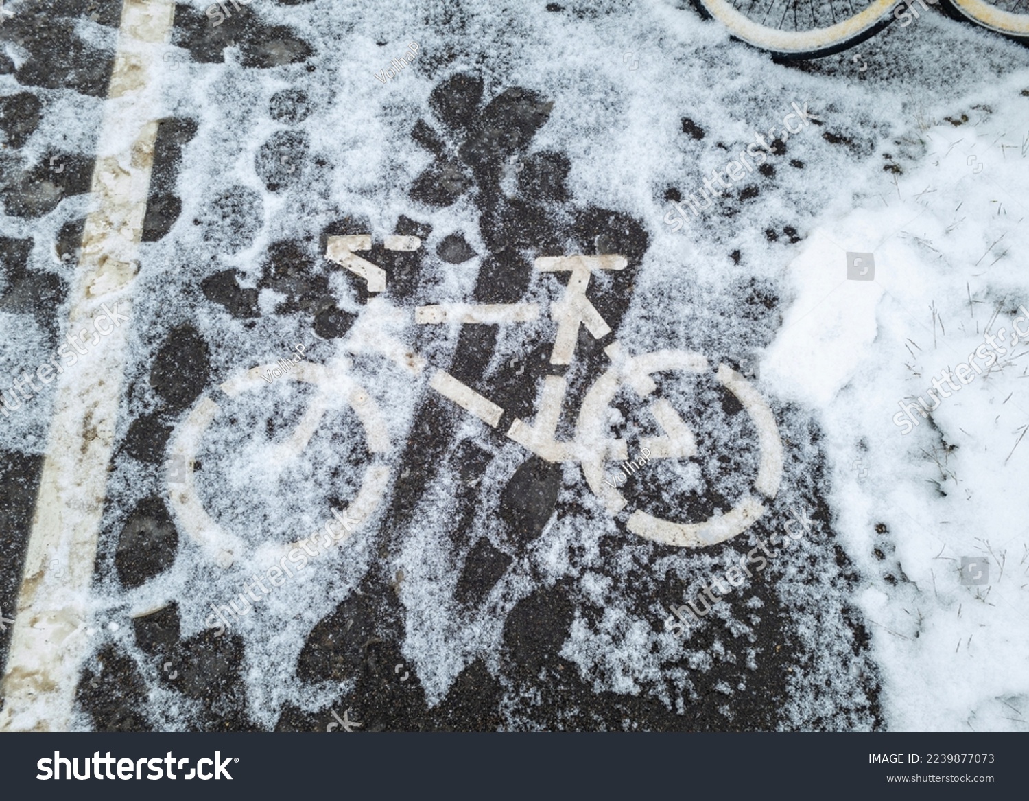 The sign of the bike path on the asphalt covered with fallen snow. Winter weather in Europe. #2239877073