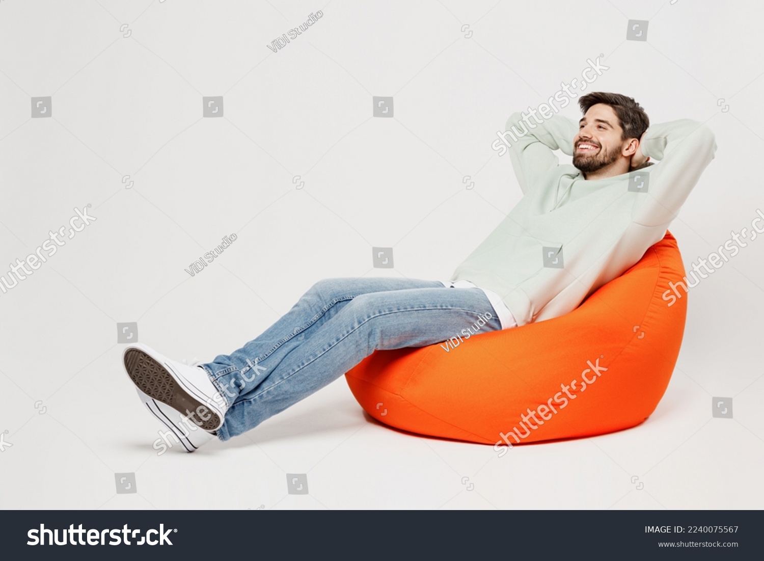 Full body young minded dreamful happy smiling man wear mint hoody sit in bag chair look camera hold hands behind neck isolated on plain solid white background studio portrait People lifestyle concept #2240075567