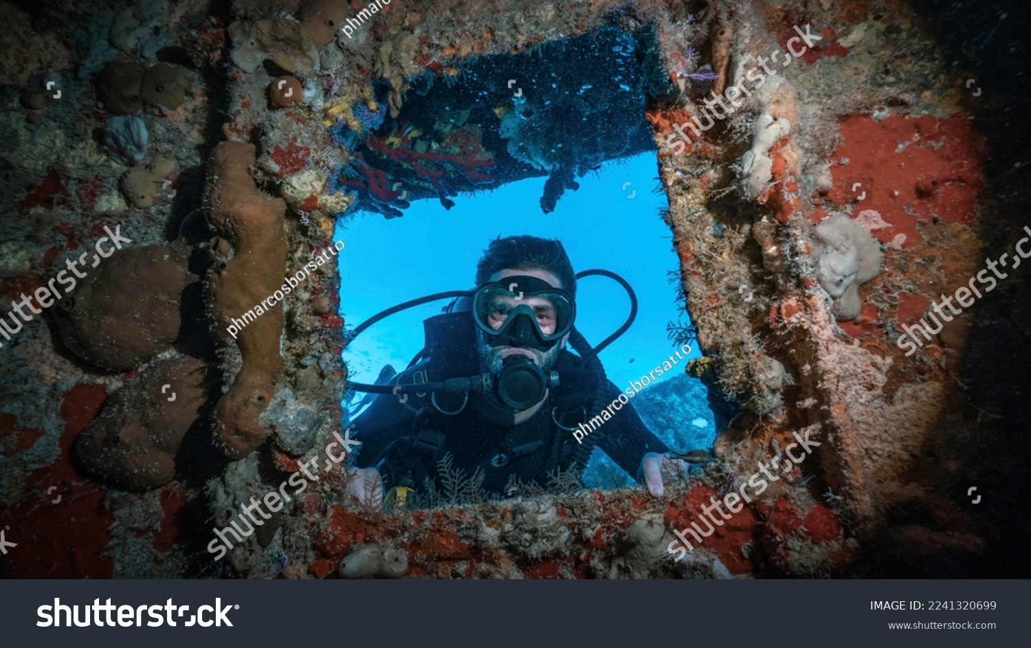 scuba diver posing in a window full of corals in a shipwreck #2241320699