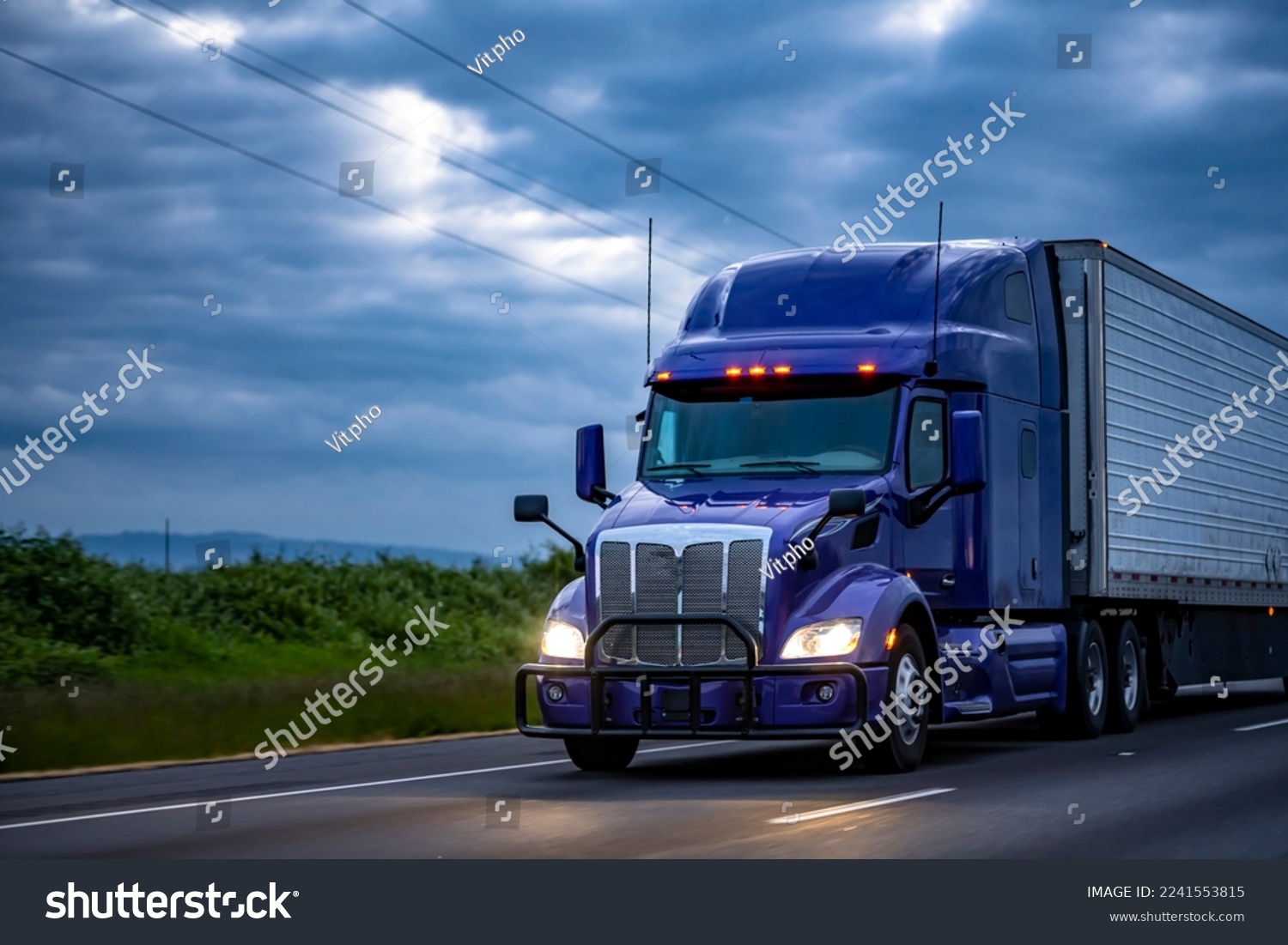 Blue industrial long haul Big rig semi truck with high cab transporting frozen commercial cargo in refrigerator semi trailer running on the evening wide highway road with storm clouds in Oregon #2241553815