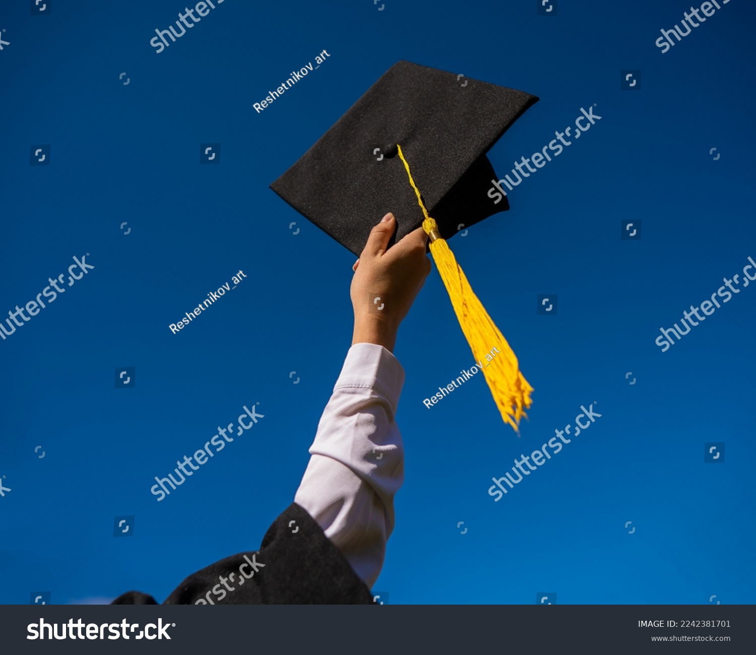 Close-up of a woman's hand with a graduation cap against the blue sky.  #2242381701