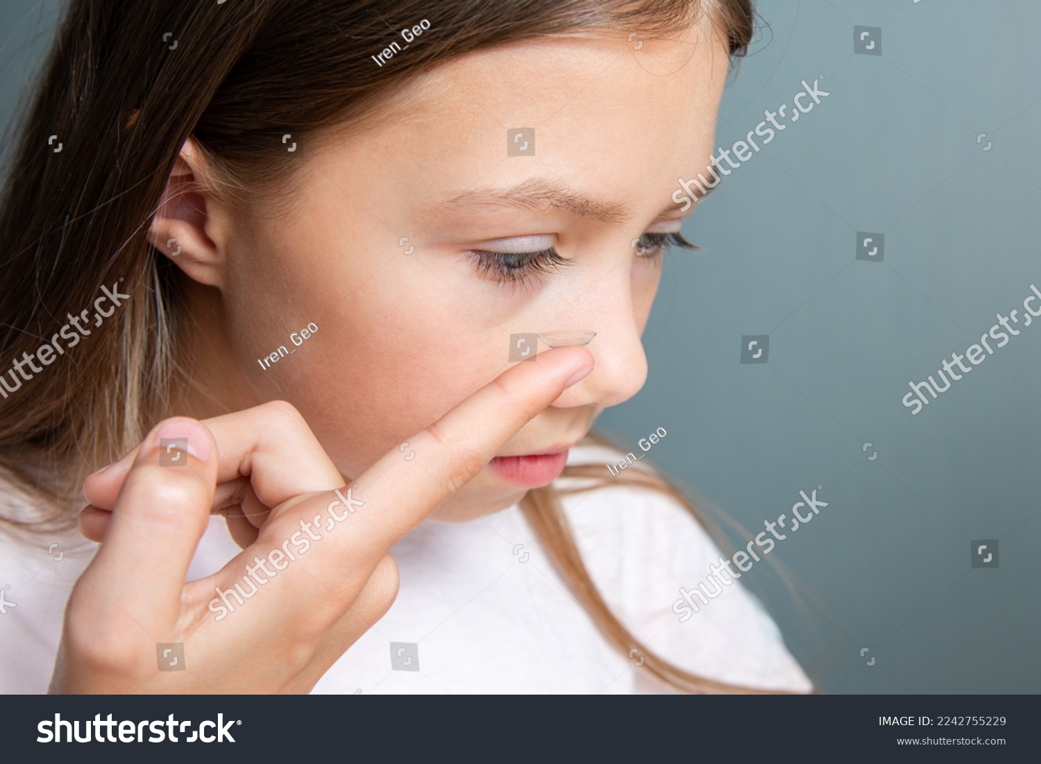 Little child girl inserting a transparent contact lens into her eye on gray background. The concept of ophthalmological poor sight correction #2242755229