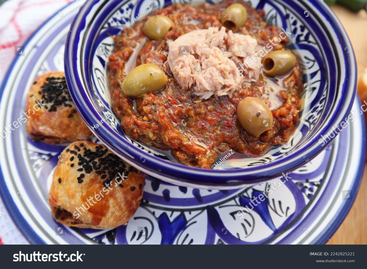 Grilled vegetables Tunisian salad with tuna and olives on top, close up view in Libyan traditional tableware with mini bread on the side  - daylight shoot  #2242825221