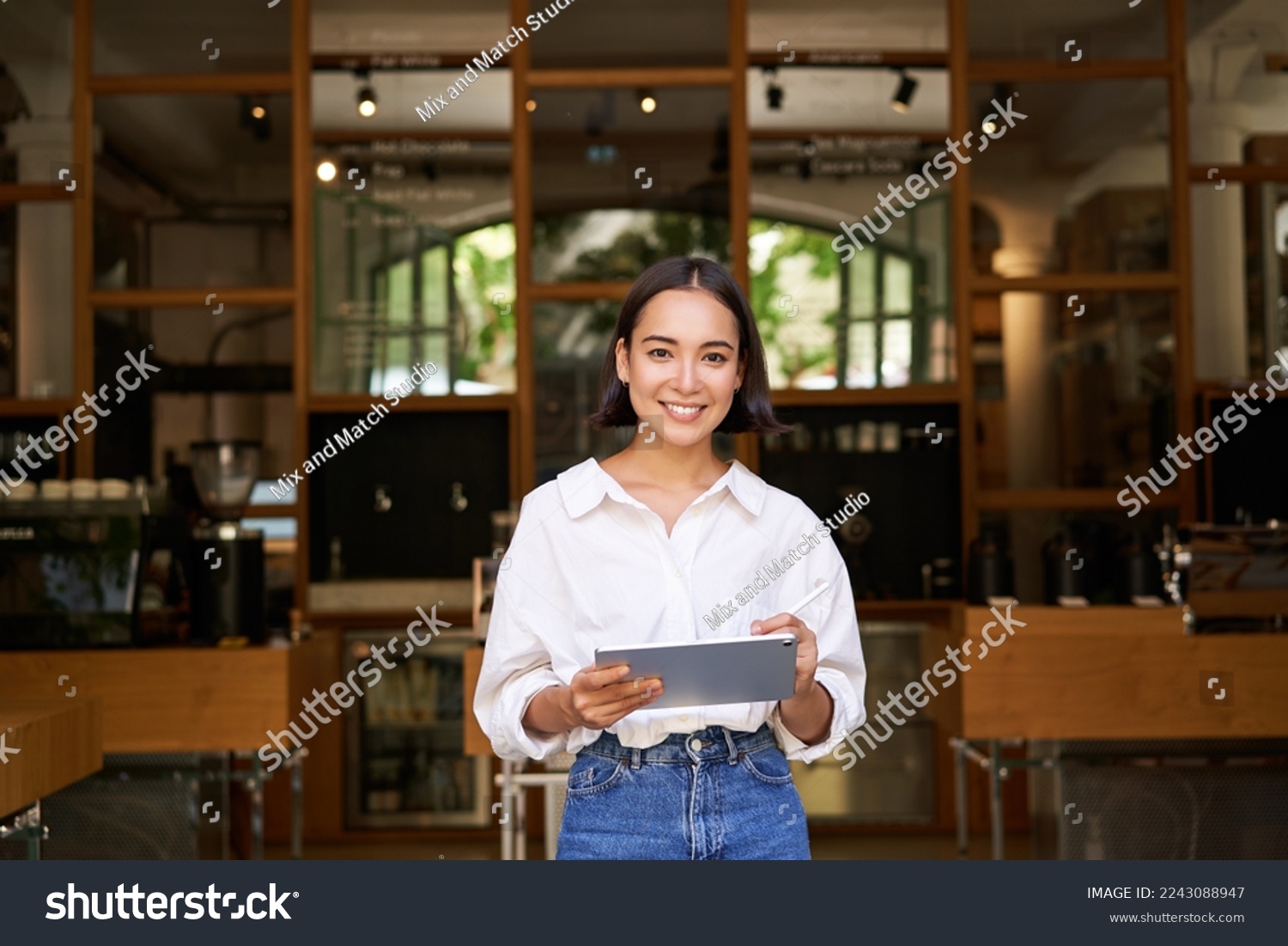 Portrait of asian woman, manager standing with tablet in front of cafe entrance, welcomes guests. Business and entrepreneurs concept #2243088947