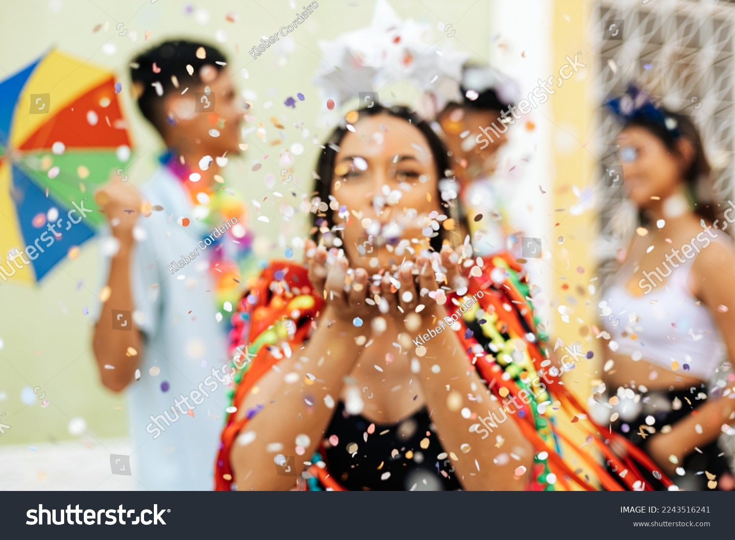 Brazilian Carnival. Group of friends celebrating carnival party. Selective focus of woman blowing confetti. #2243516241
